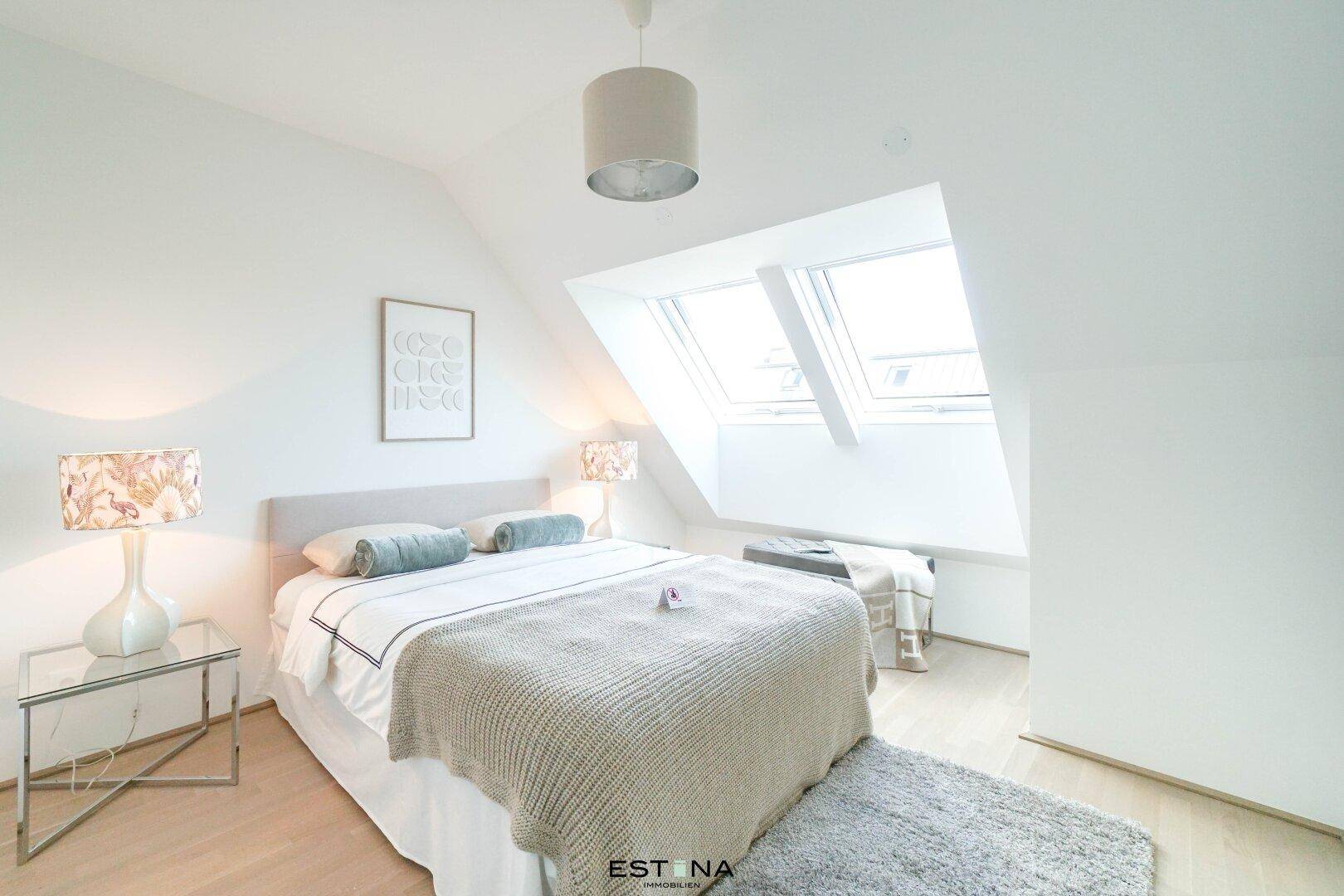 Helles Schlafzimmer im Dachgeschoss mit Doppelbett, Dachfenstern und Holzboden.