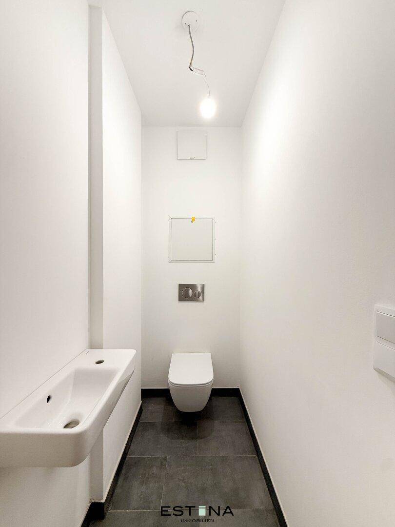 Separates WC mit wandhängender Toilette und kleinem Handwaschbecken.