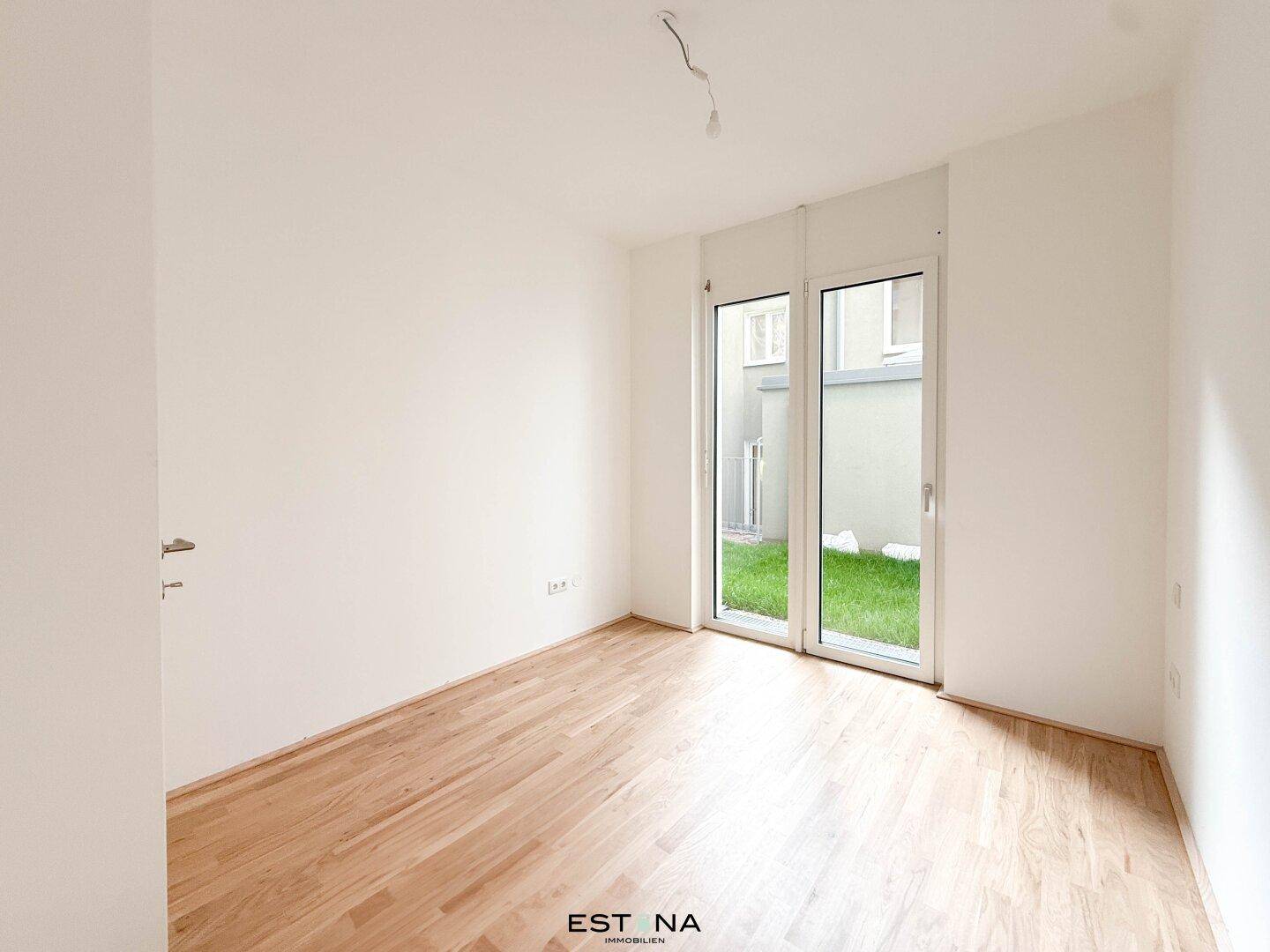 Weiteres helles Zimmer mit Holzboden und Zugang zu einem kleinen Außenbereich.