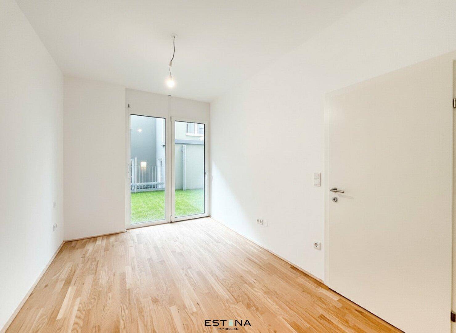 Helles Zimmer mit Holzboden und direktem Zugang zu einer kleinen Grünfläche.