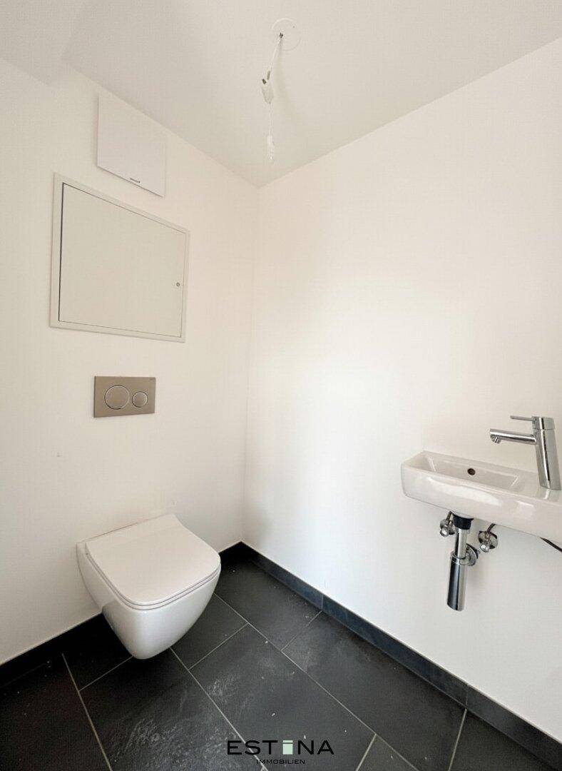 Separates Gäste-WC mit wandhängender Toilette und kleinem Handwaschbecken.