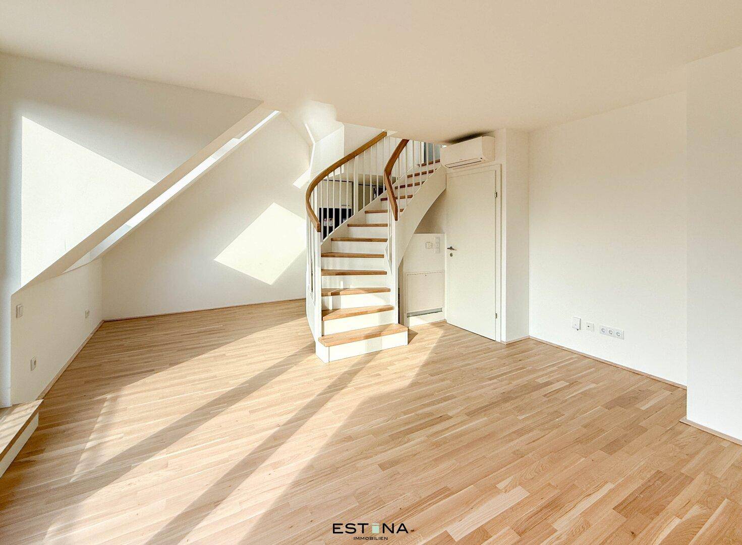 Heller Wohnbereich mit Holzfußboden, Dachschräge und Zugang zur oberen Etage über eine Wendeltreppe.