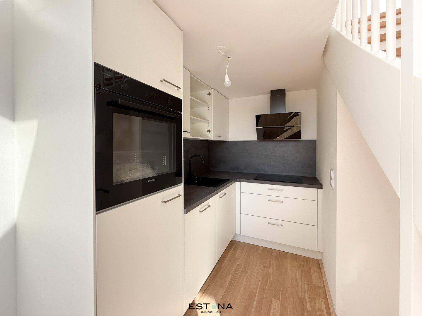 Moderne Einbauküche mit weißen Fronten, integriertem Backofen und dunkler Arbeitsplatte.