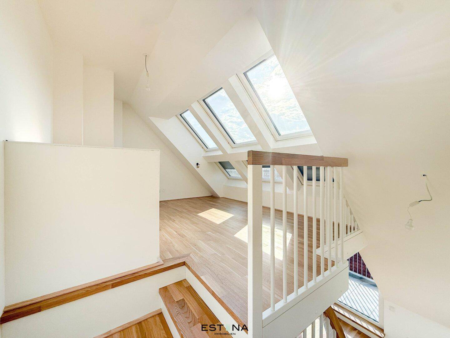Blick vom oberen Geschoss in den hellen Wohnbereich mit Holztreppe und Dachfenstern.