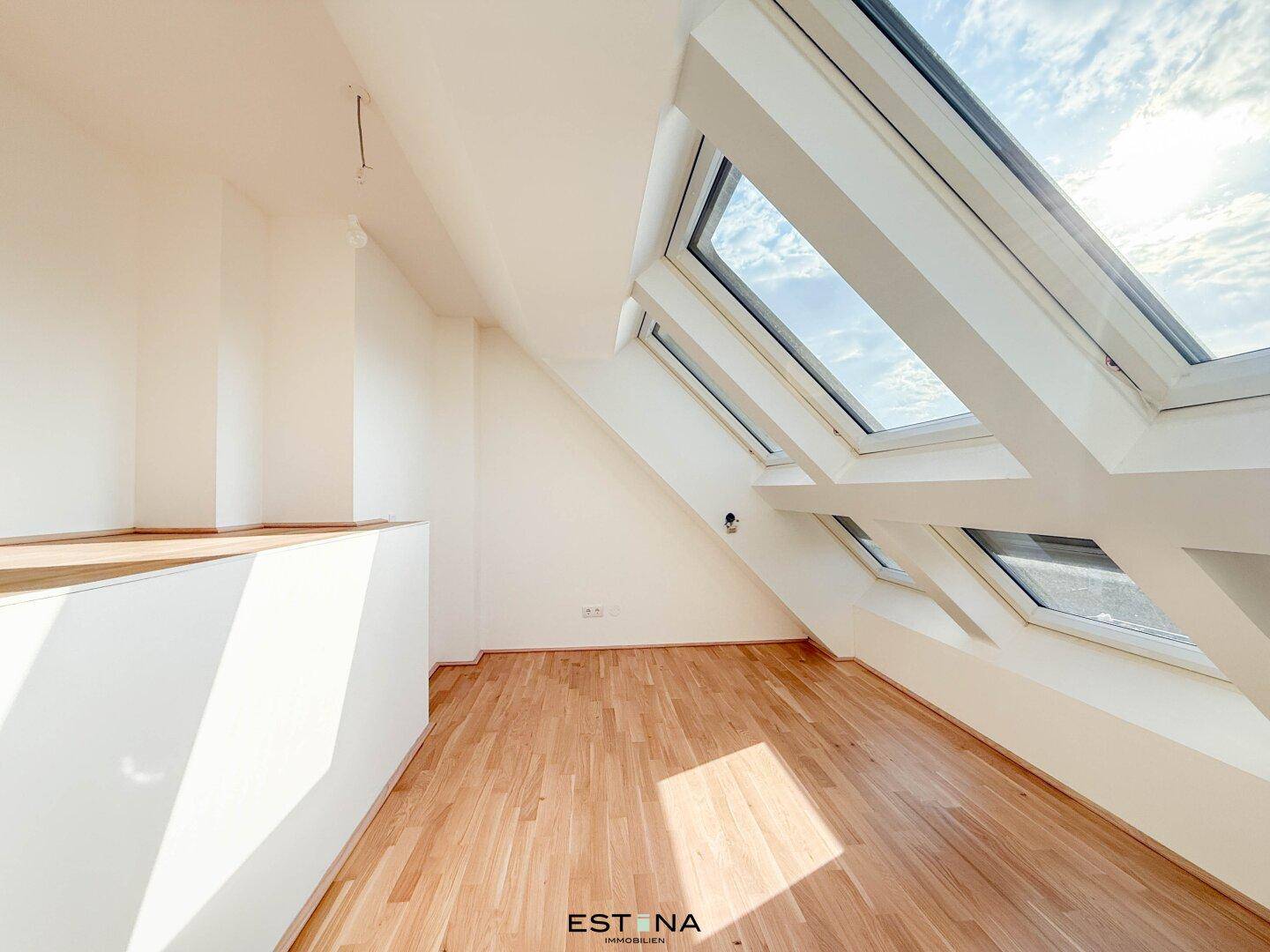 Lichtdurchfluteter Dachgeschossraum mit schrägen Wänden und großen Dachfenstern.
