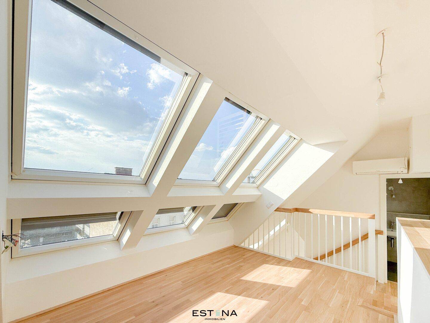 Heller Raum im Dachgeschoss mit mehreren Dachfenstern und Blick auf den Himmel.