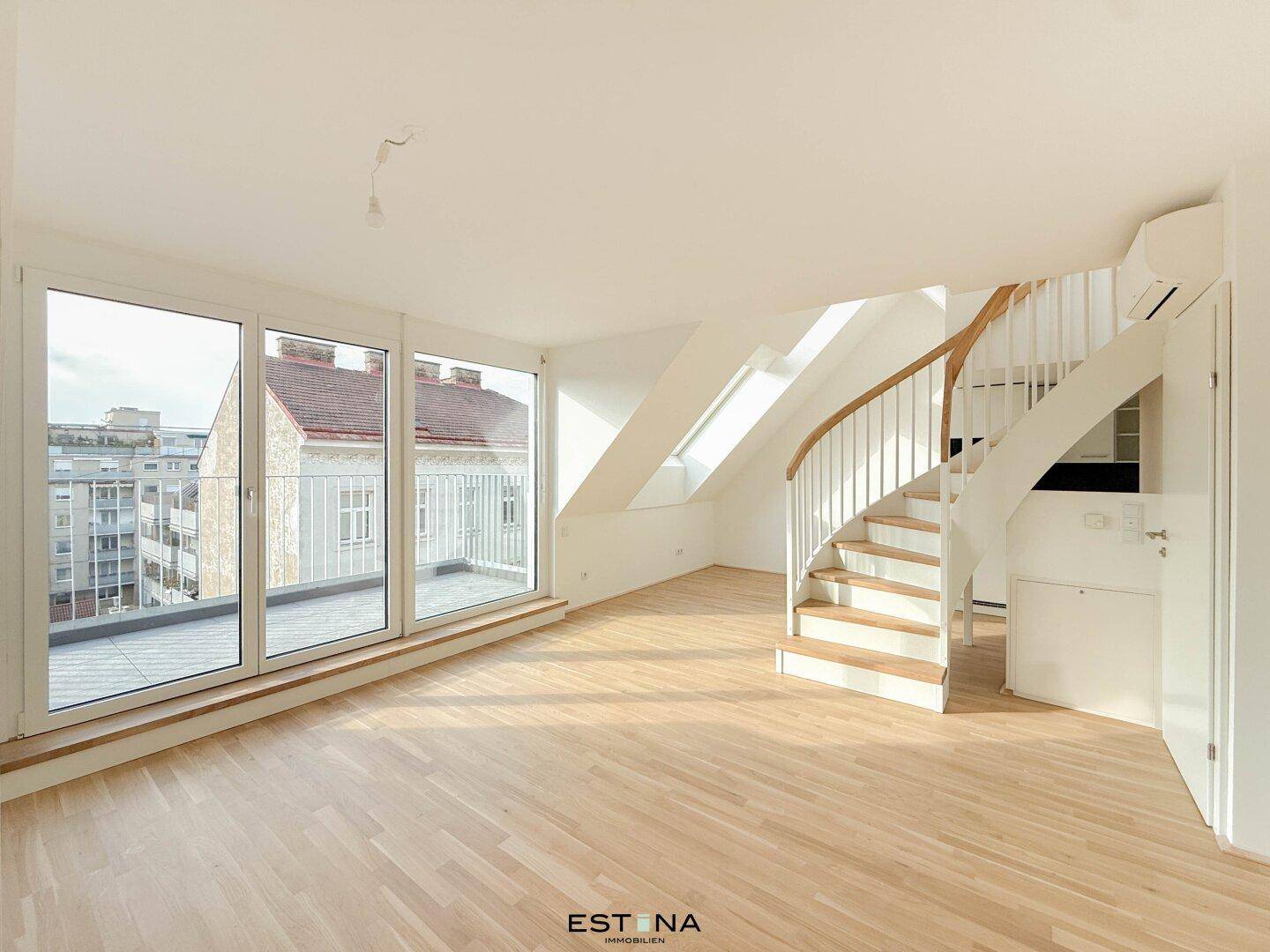 Lichtdurchfluteter Wohnbereich mit großen Fenstern, Dachschrägen und Wendeltreppe.