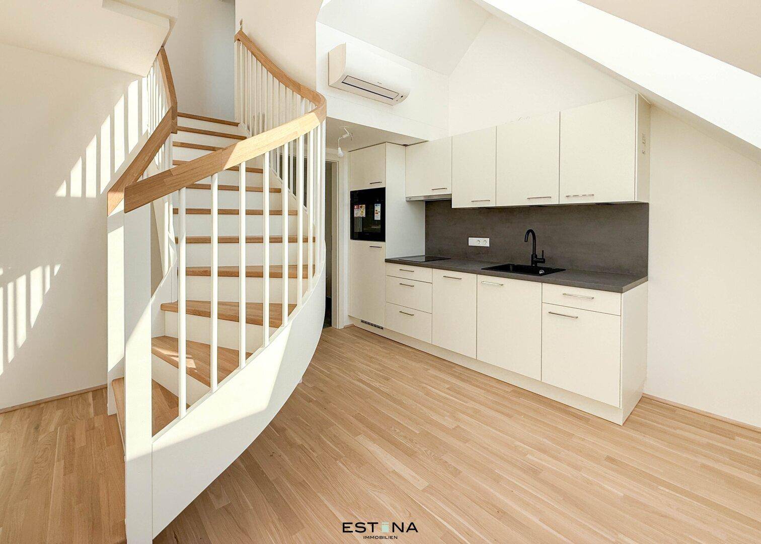 Moderne Küchenzeile im Dachgeschoss mit weißen Schränken, dunkler Arbeitsplatte und Holzparkett.