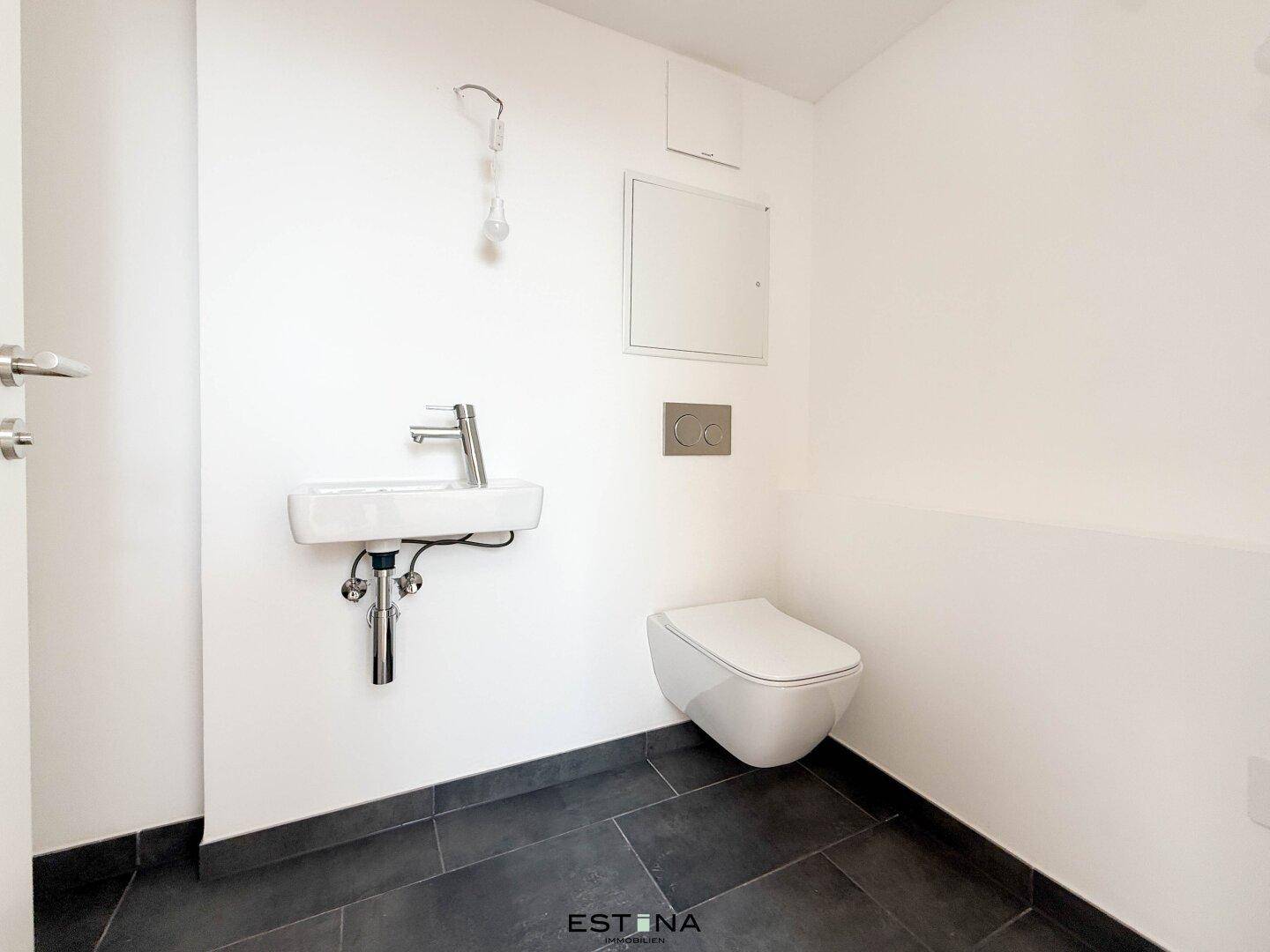 Separates Gäste-WC mit modernem Waschbecken, wandhängendem WC und dunklem Fliesenboden.