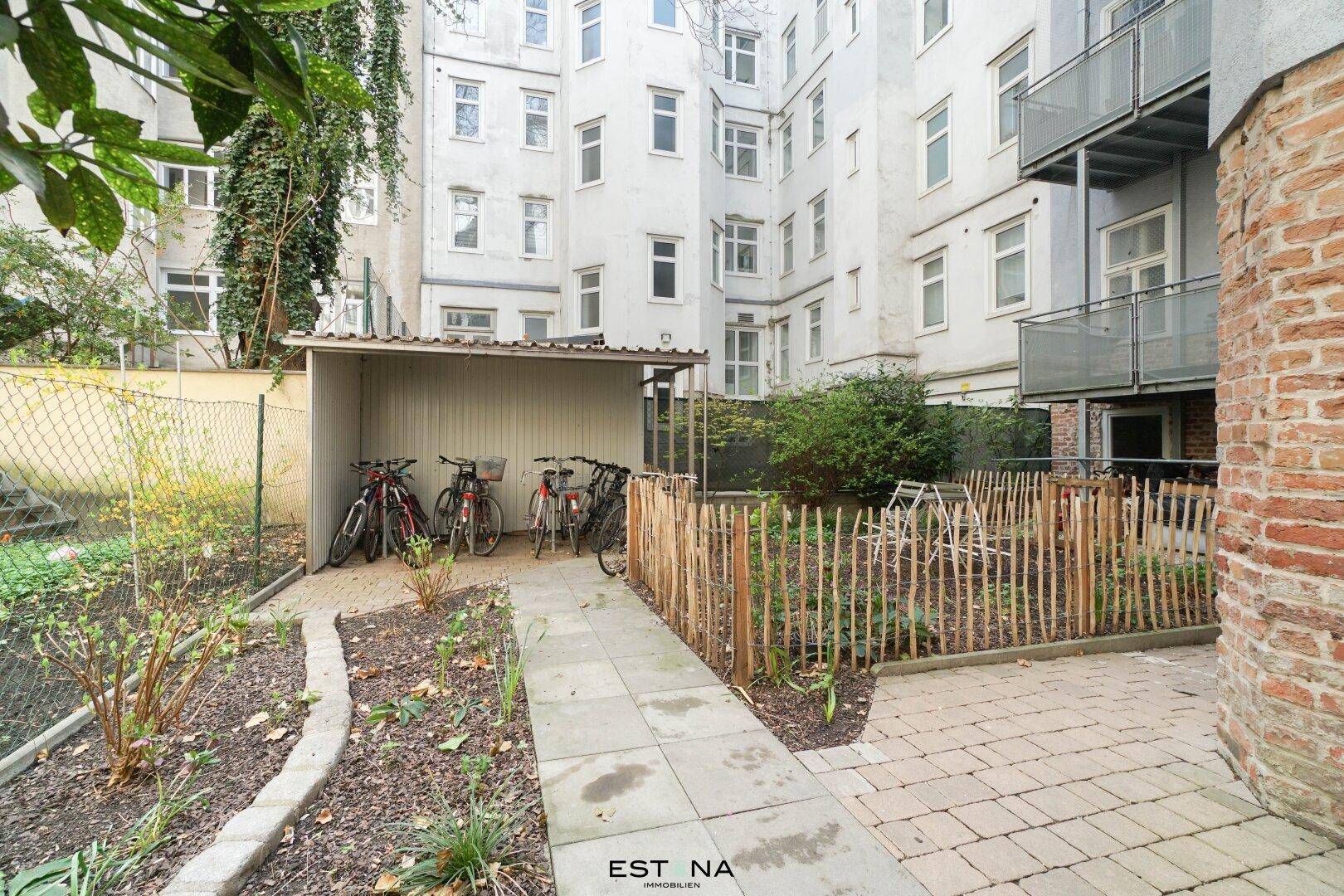 Gemeinschaftsgarten mit Fahrradunterstand, gepflastertem Weg und begrünten Beeten im Innenhof.