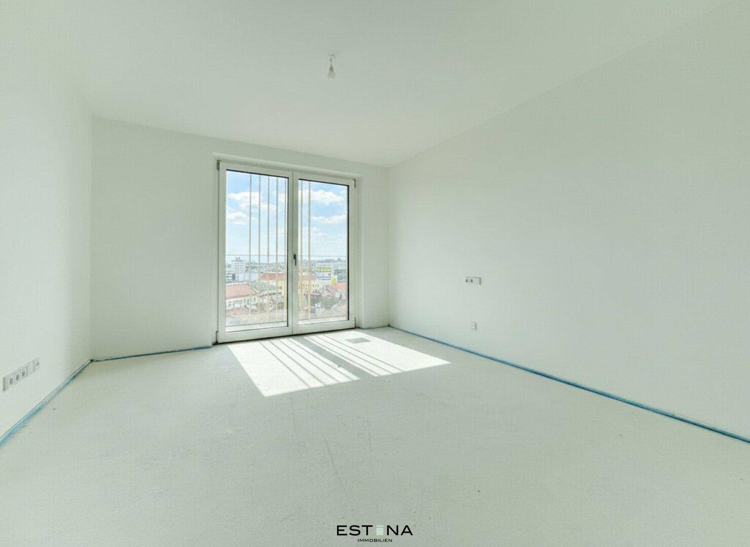 Unmöbliertes Schlafzimmer mit großem Fenster und Rohbau-Boden, bietet viel Tageslicht und Stadtblick.