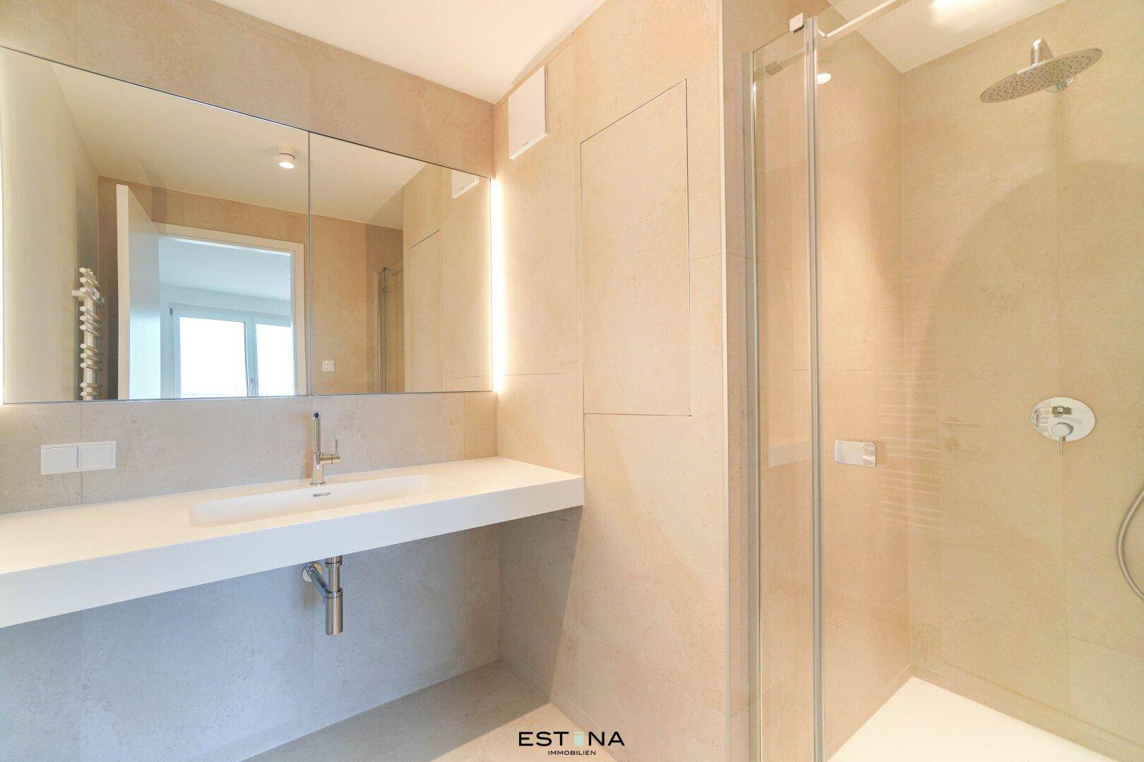 Modernes Badezimmer mit großem Spiegel, Einzelwaschbecken und begehbarer Dusche in hellen Beigetönen.