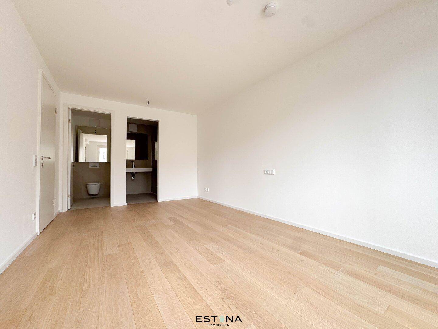 Geräumiges Zimmer mit Holzboden und Zugang zu einem modernen Badezimmer.
