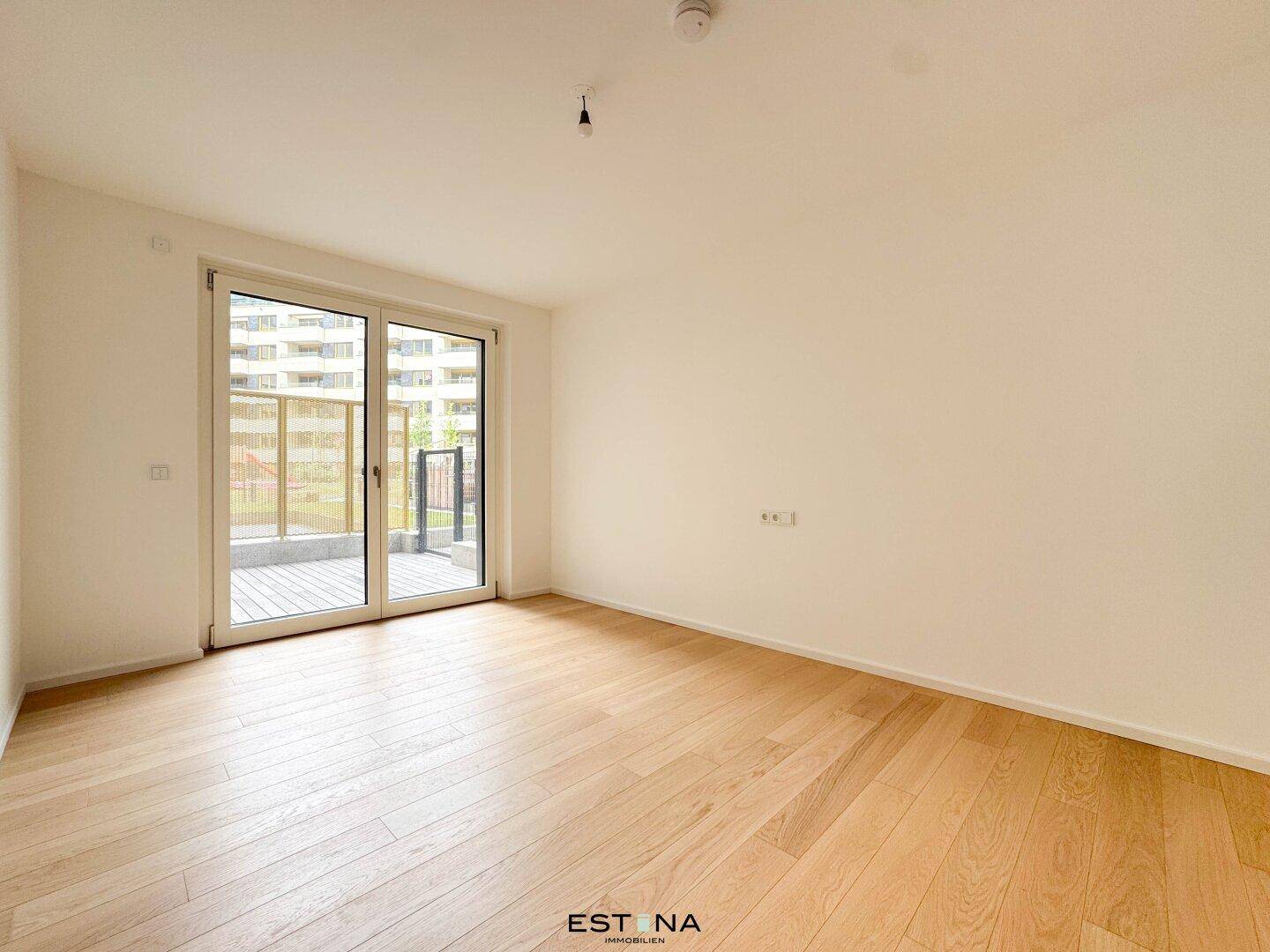 Helles Zimmer mit Holzboden und großem Fenster, das Zugang zu einem Außenbereich bietet.