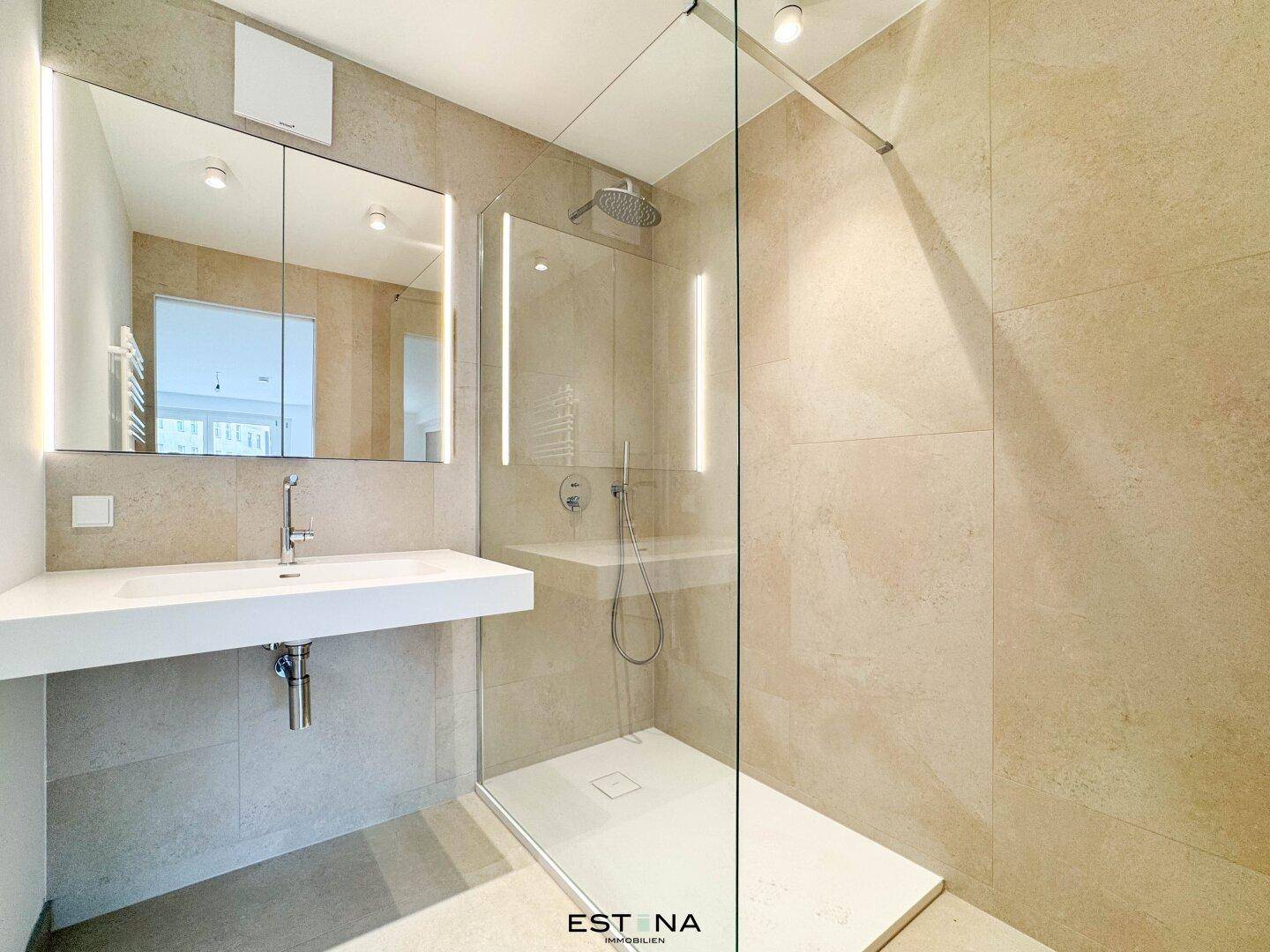 Elegantes Badezimmer mit begehbarer Dusche, großem Spiegel und hellen Fliesen.