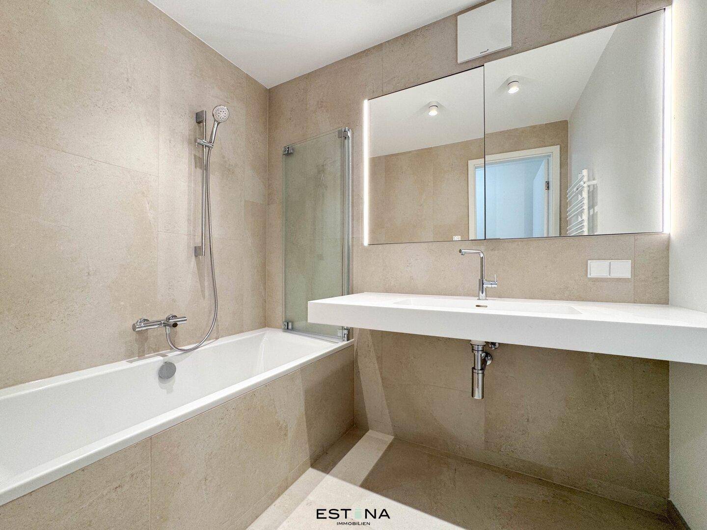 Modernes Badezimmer mit Badewanne, großem Spiegel und beigefarbenen Fliesen.