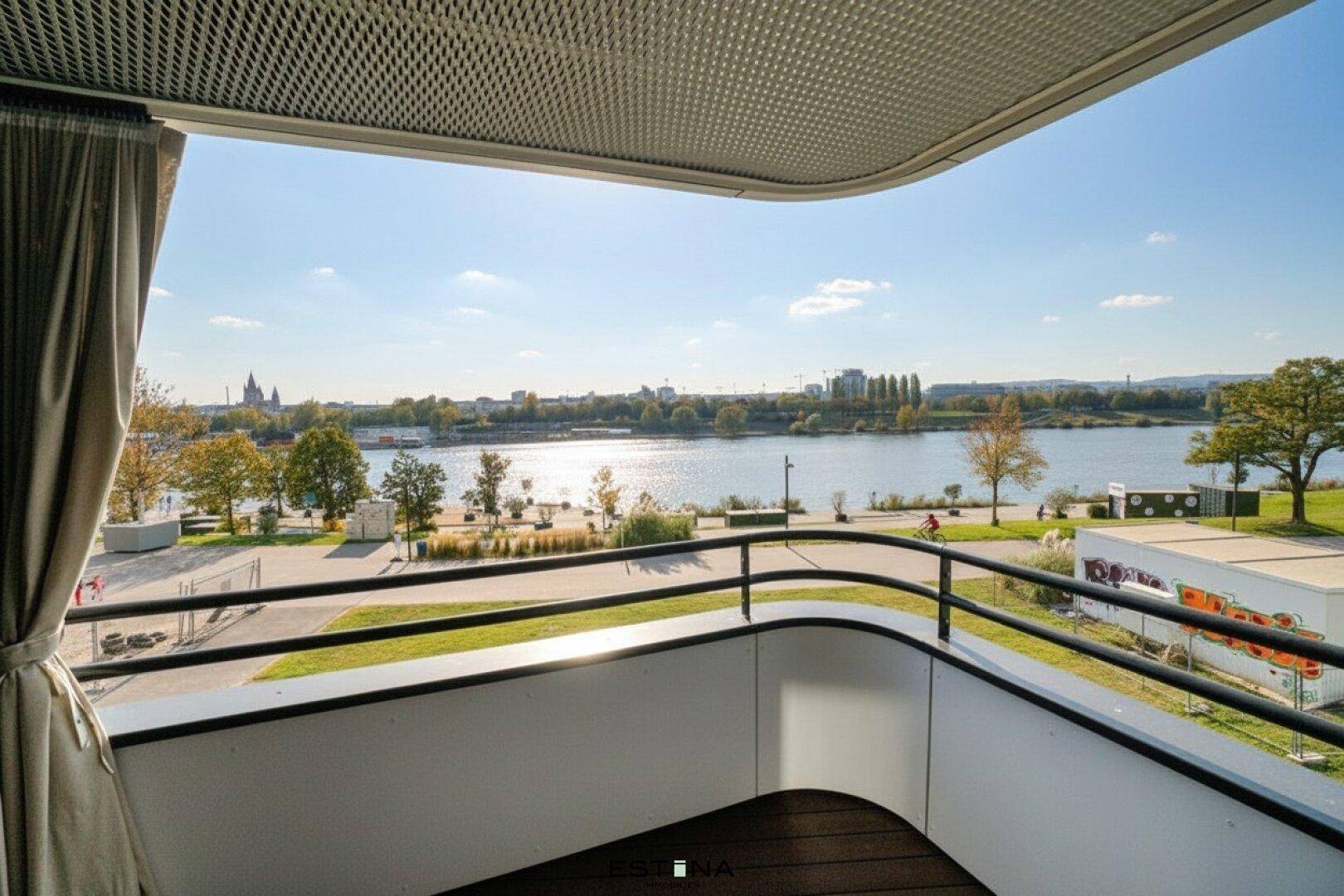 Sonniger Balkon mit Holzboden und weitem Blick auf den Fluss und die Stadt.