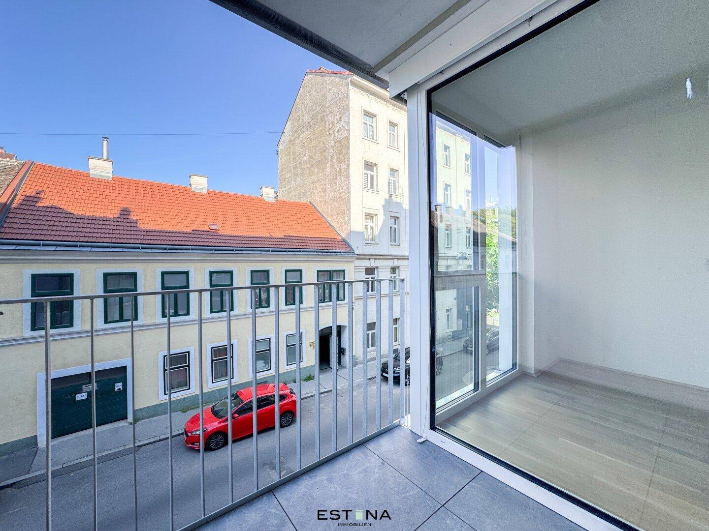 Balkon mit Metallgeländer und Blick auf die gegenüberliegenden Gebäude und die Straße.