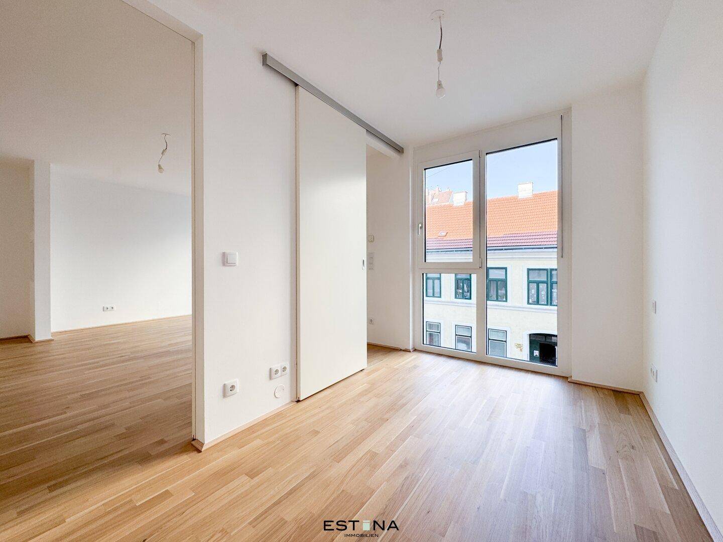 Helles Zimmer mit Parkettboden, großen Fenstern und einer modernen Schiebetür.
