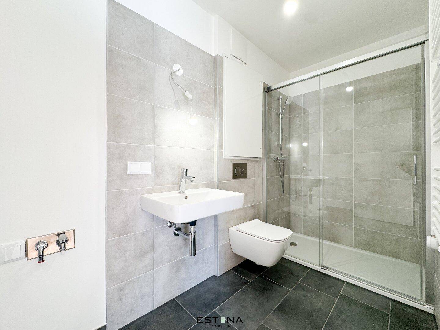Modernes Badezimmer mit grauen Fliesen, ebenerdiger Dusche und wandhängendem WC.