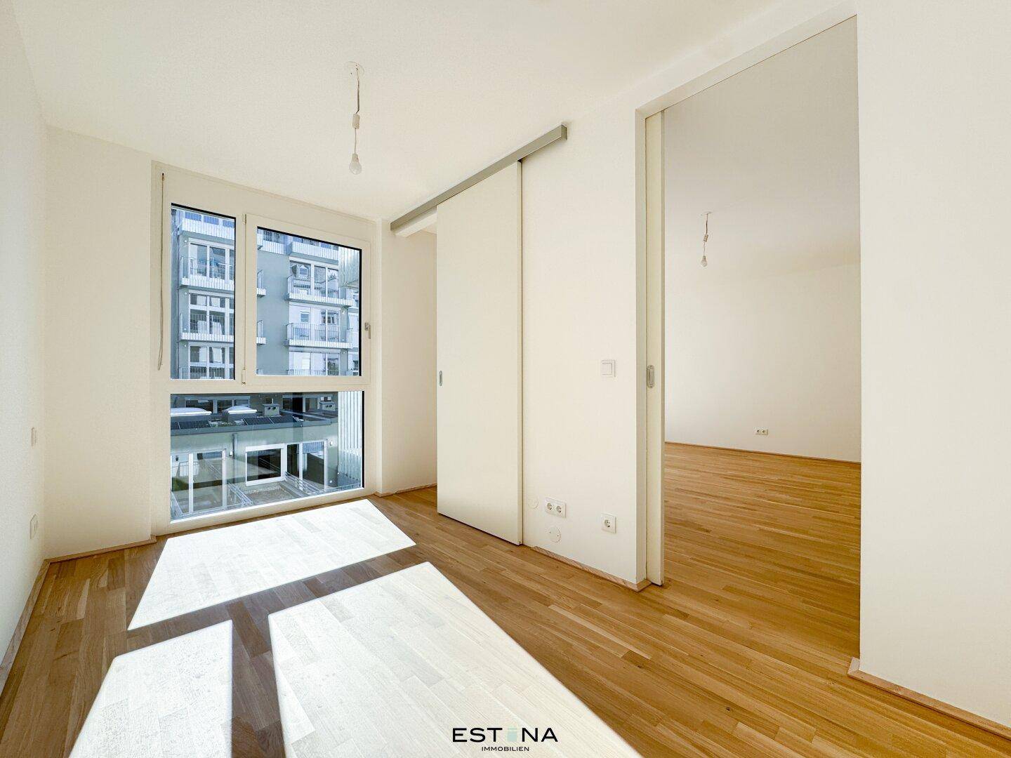Lichtdurchfluteter Raum mit großen Fenstern, Parkettboden und moderner Schiebetür.