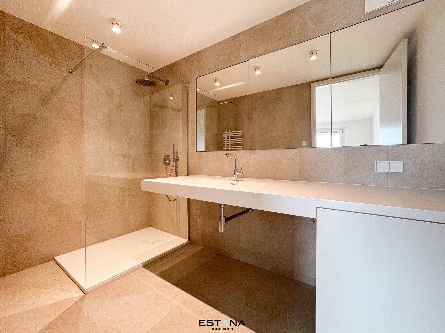 Modernes Badezimmer mit großer begehbarer Dusche, eleganten Fliesen und breitem Waschtisch mit Spiegel.