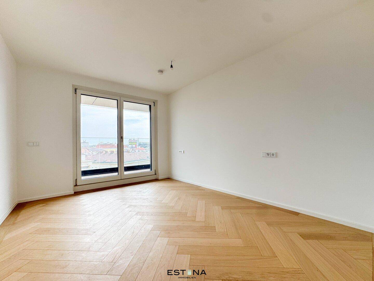 Helles Zimmer mit Fischgrätparkett und Zugang zu einem Balkon, bietet einen weiten Ausblick.