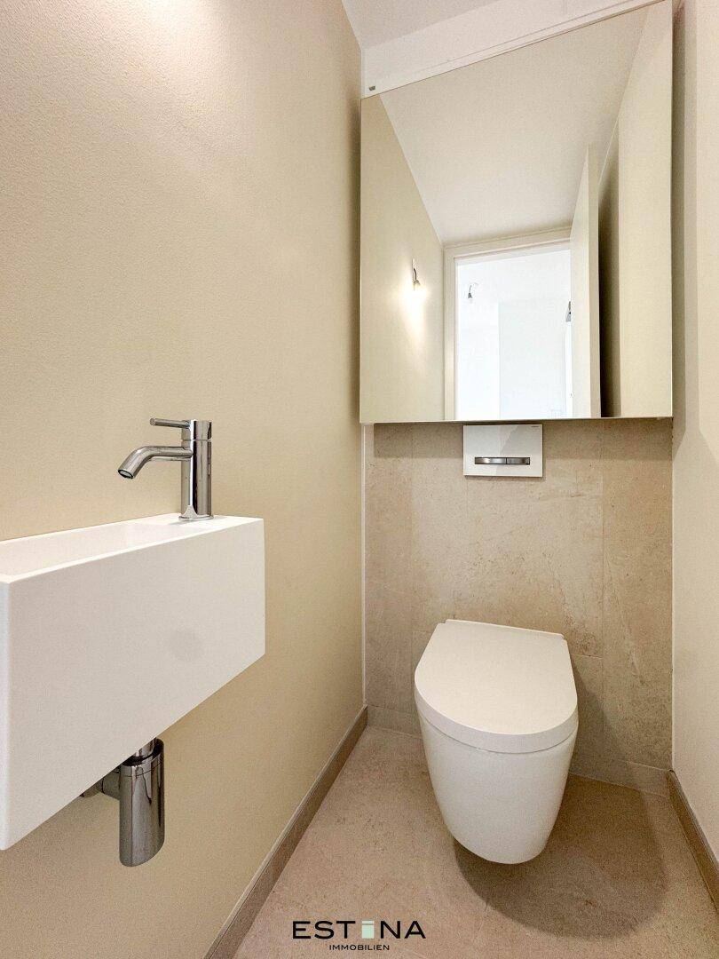 Kompaktes Gäste-WC mit modernem Wand-WC, kleinem Waschbecken und Spiegel, in neutralen Farbtönen gehalten.