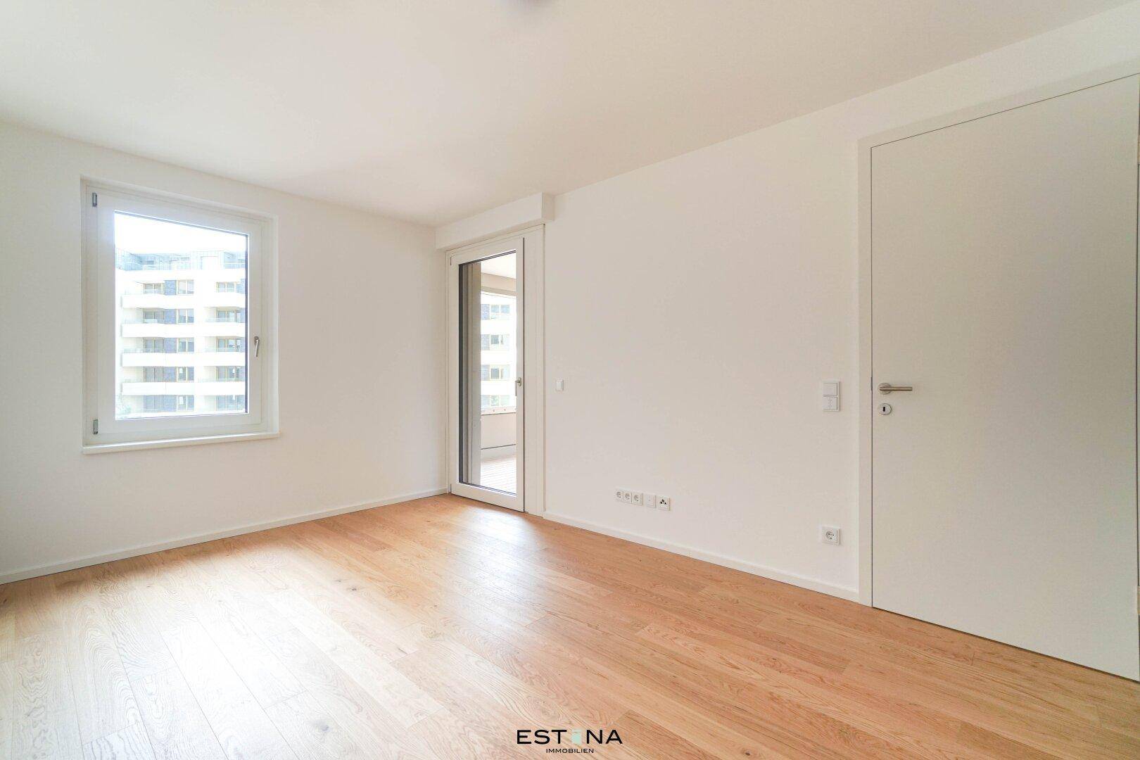Helles Schlafzimmer mit Parkettboden, großem Fenster und Zugang zu einem Außenbereich.