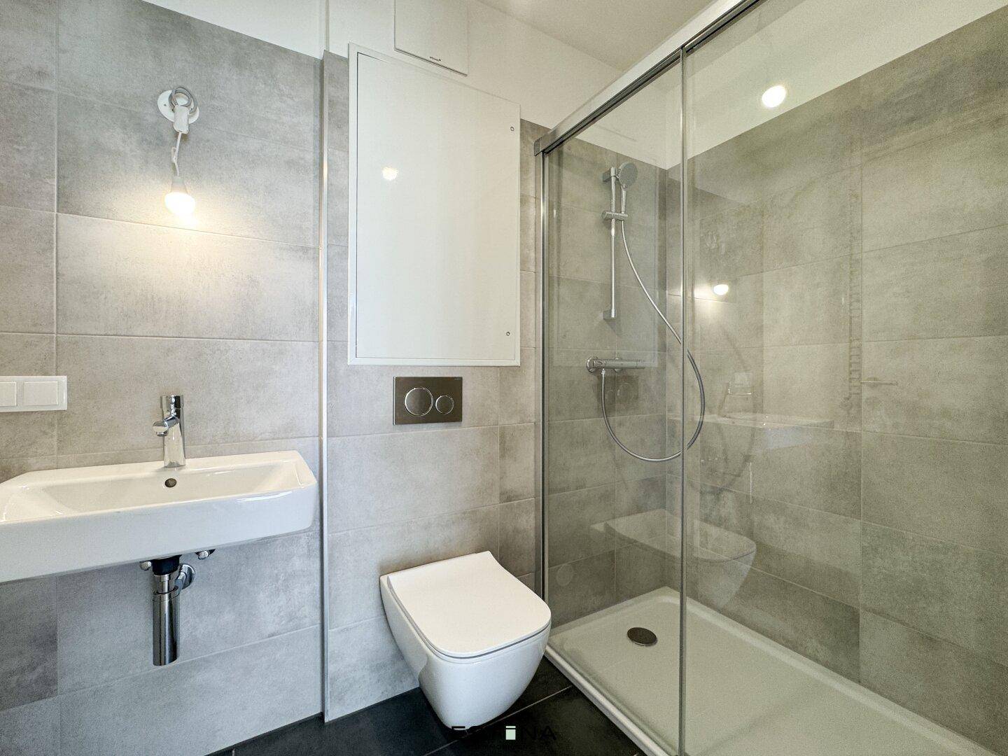 Modernes Badezimmer mit grauen Fliesen, wandhängendem WC und begehbarer Dusche.