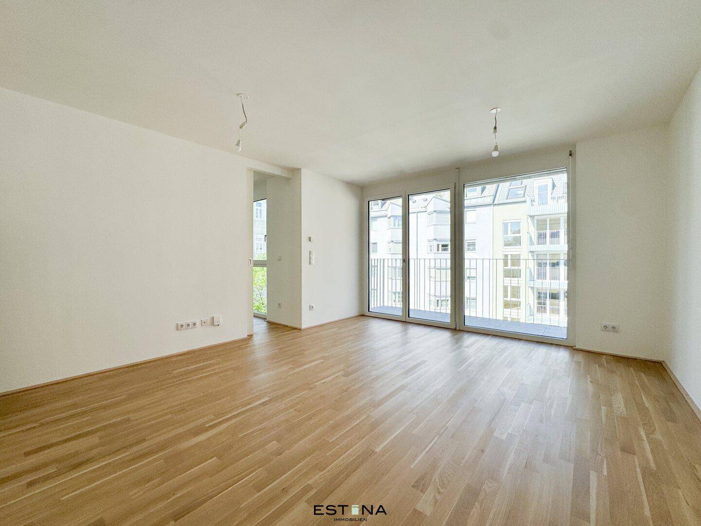 Lichtdurchfluteter Wohnbereich mit großen Fenstern und Zugang zu einem französischen Balkon.