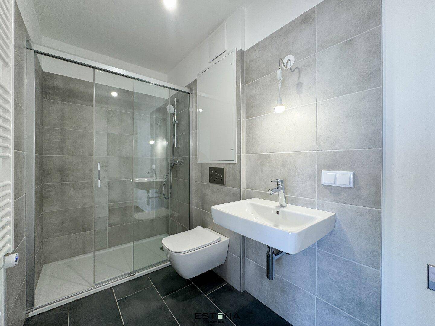 Modernes Badezimmer mit grauen Fliesen, ebenerdiger Dusche und wandhängendem WC.