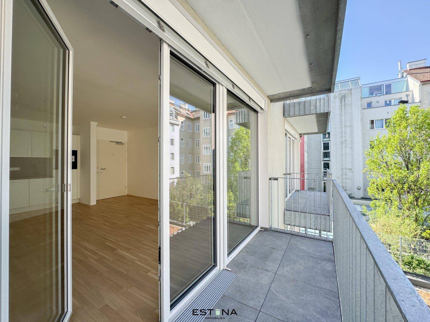Geräumiger Balkon mit Fliesenboden und Blick auf die umliegenden Gebäude und Bäume.