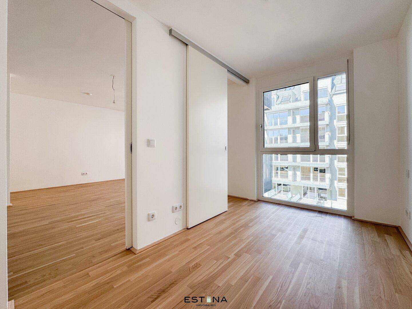 Helles Zimmer mit Parkettboden, großen Fenstern und Schiebetür, ideal als Schlaf- oder Arbeitszimmer.