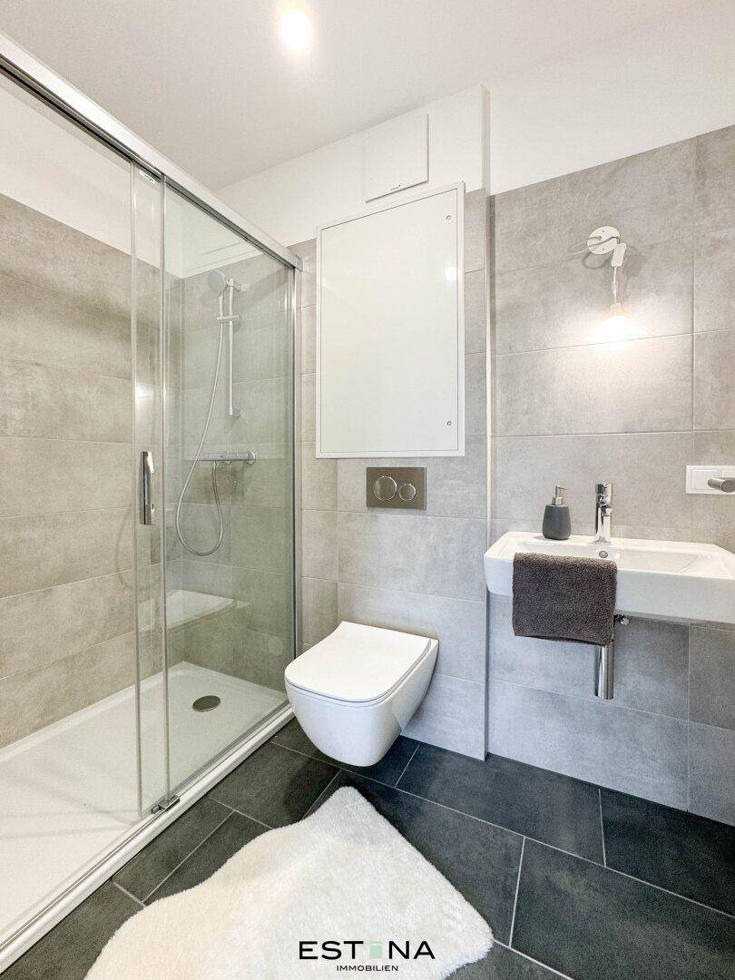 Zeitgemäßes Badezimmer mit grauen Fliesen, wandhängendem WC und ebenerdiger Dusche.