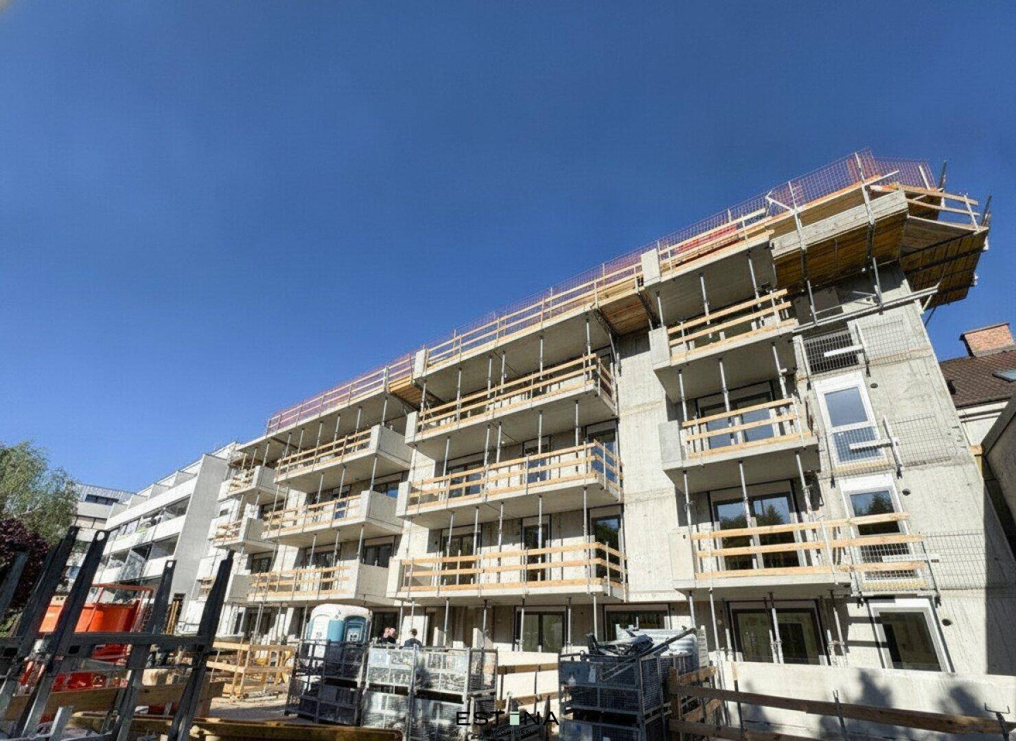 Neubauwohnungskomplex im Bau mit sichtbaren Balkonen und Gerüst unter blauem Himmel.