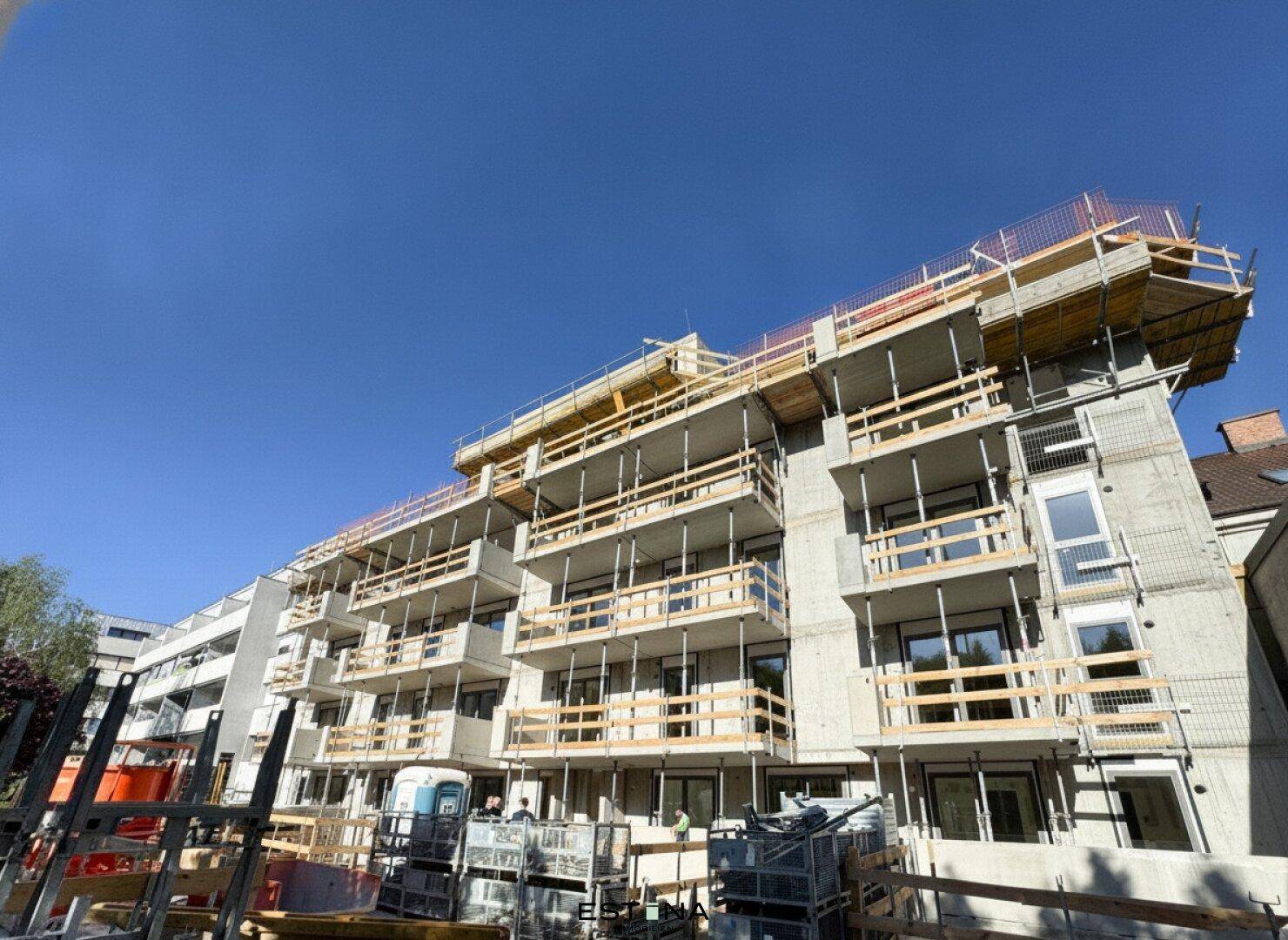 Neubau in der Bauphase mit Gerüst und sichtbaren Balkonen unter blauem Himmel.