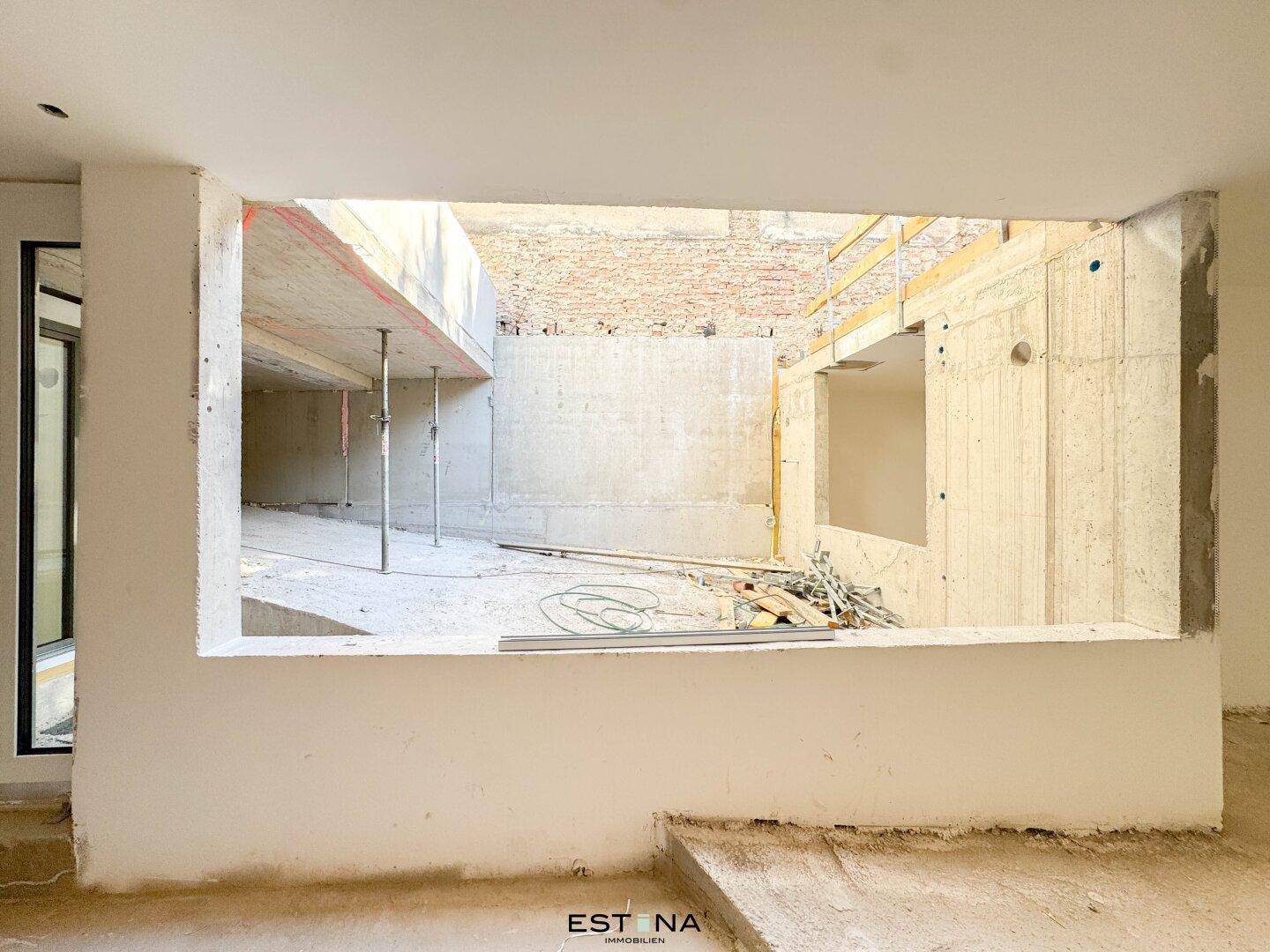 Blick aus einem unfertigen Raum auf die Rohbau-Struktur des Gebäudes und die Baustelle.