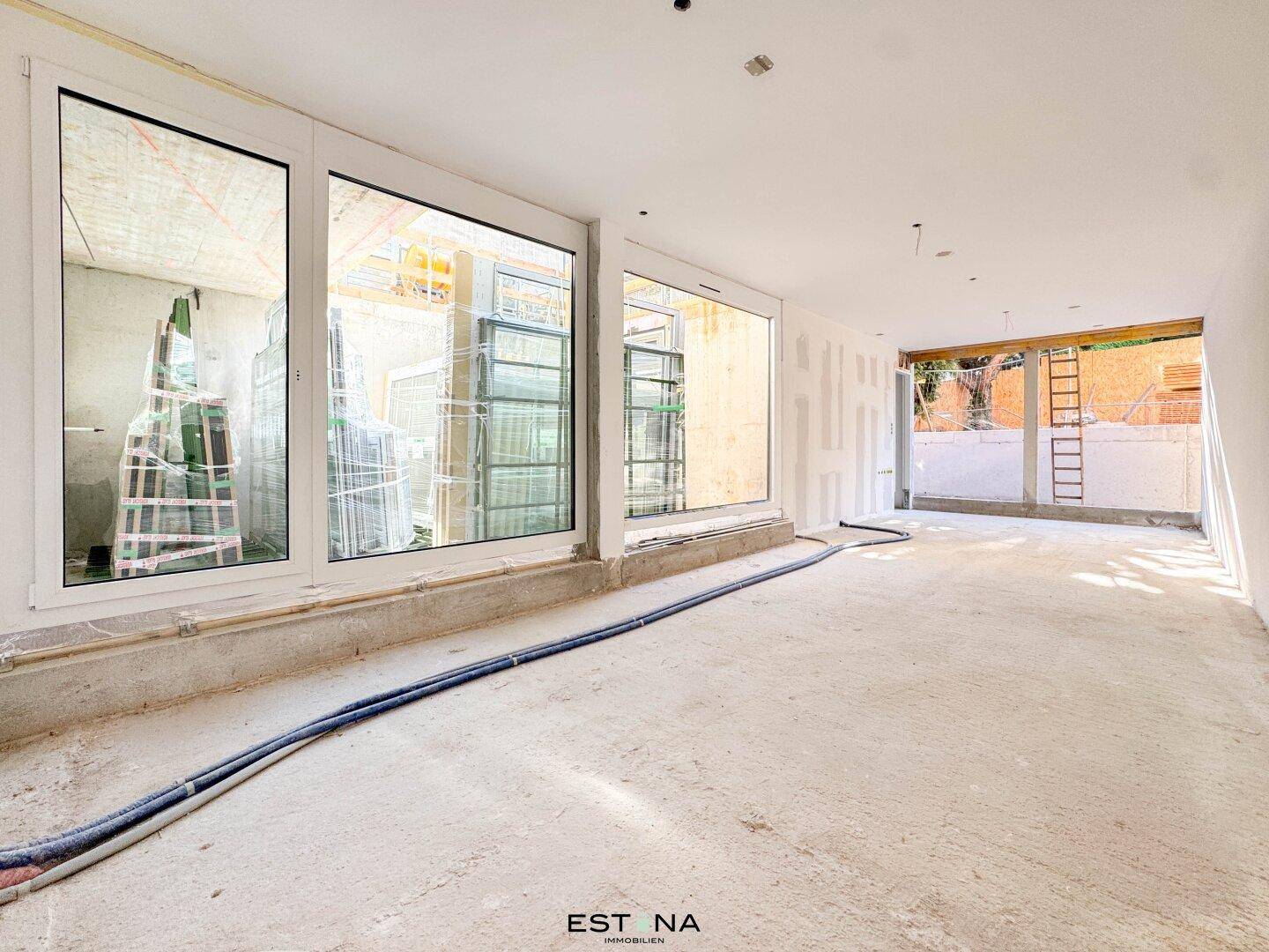 Innenraum im Rohbau mit großen Fenstern und sichtbaren Installationen, bereit für den weiteren Ausbau.