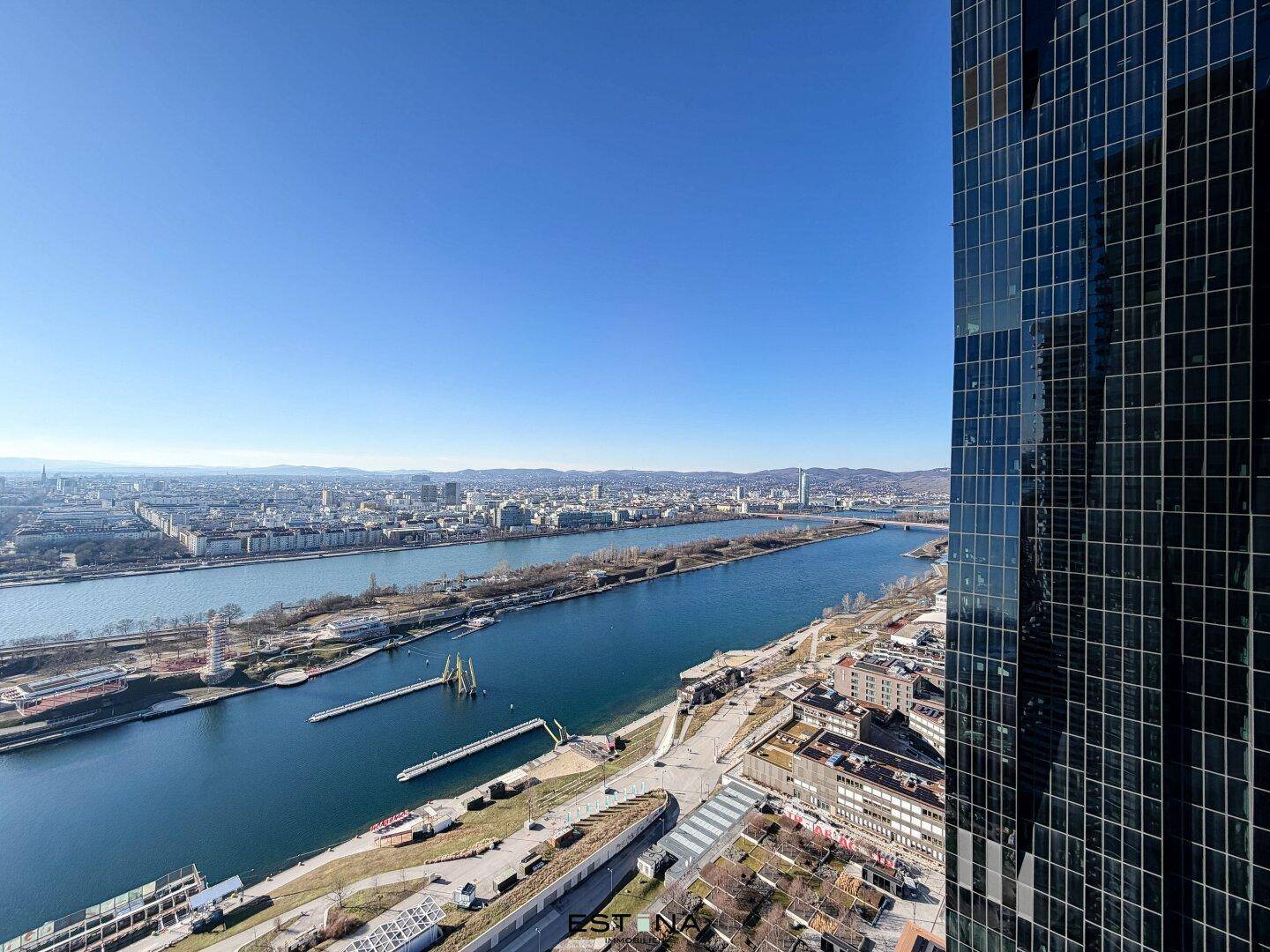 Panoramablick auf die Stadt mit Fluss, Brücke und einem modernen Glasfassaden-Hochhaus.