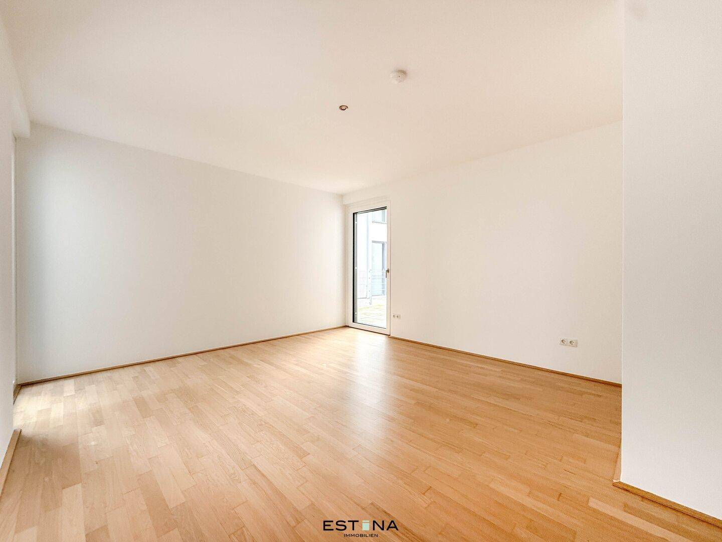 Helles Schlafzimmer mit Parkettboden, weißen Wänden und Zugang zu einem französischen Balkon.