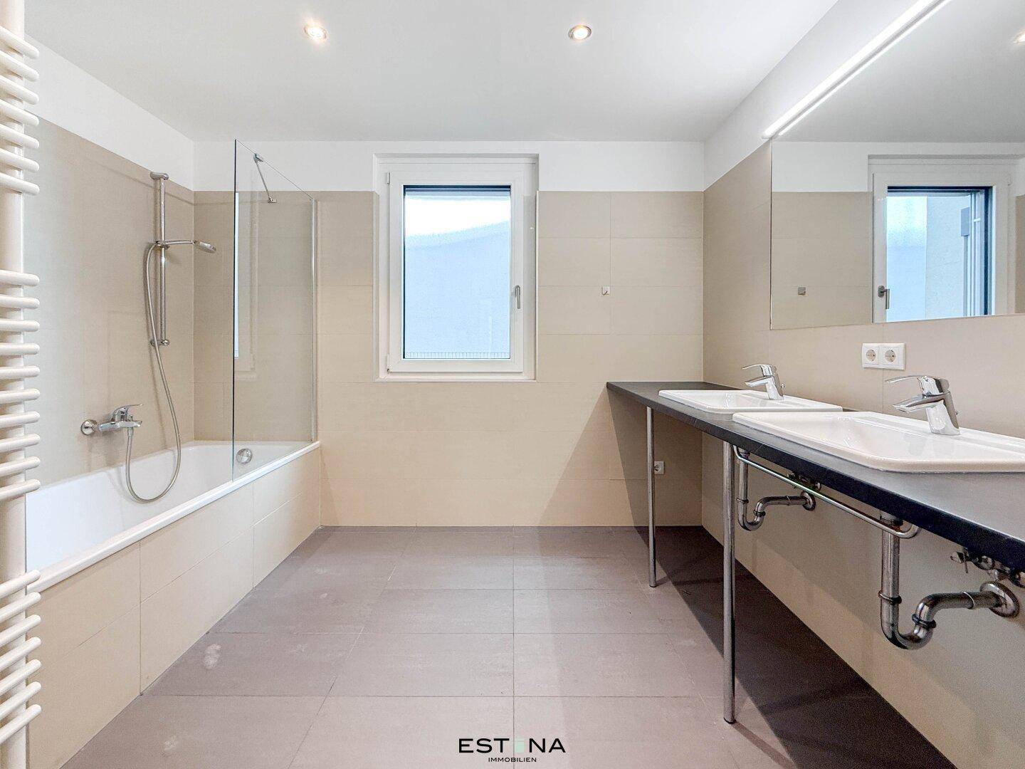 Modernes Badezimmer mit Doppelwaschbecken, Badewanne mit Duschbereich und beheiztem Handtuchhalter.