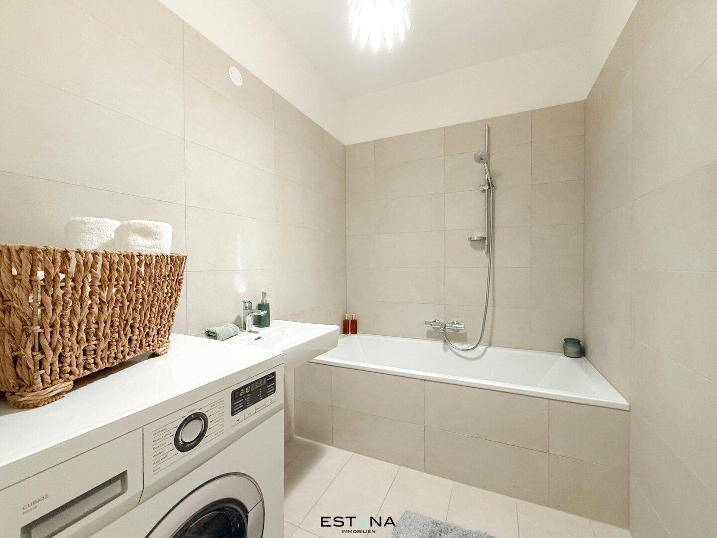 Modernes Badezimmer mit Badewanne, Waschmaschine und hellen Fliesen.