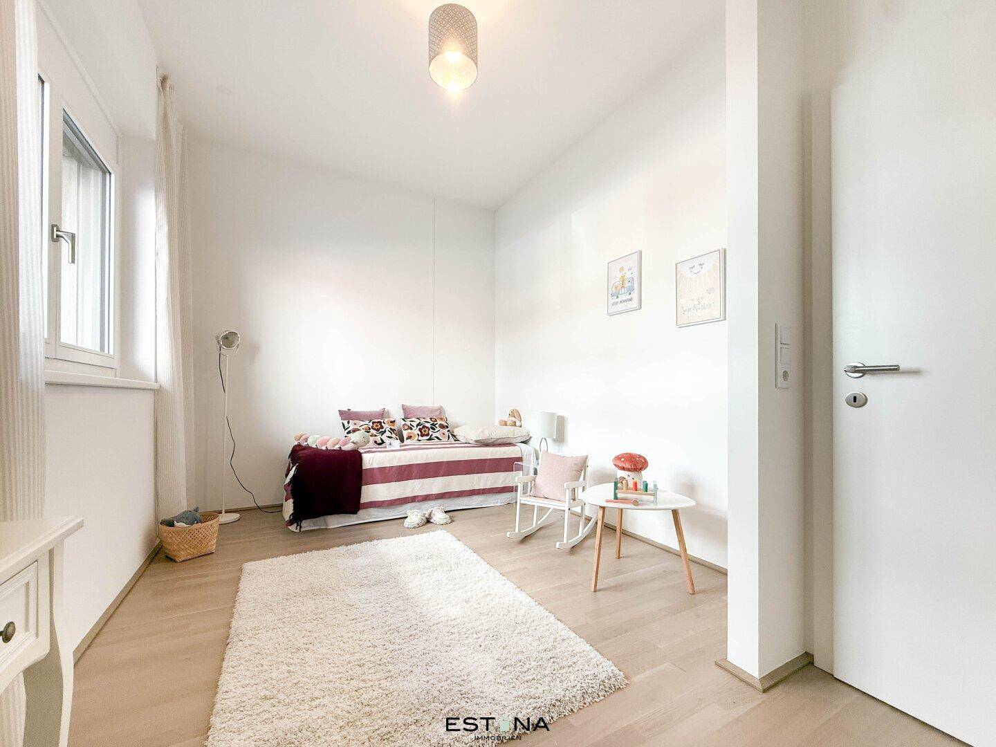 Freundliches Kinderzimmer mit Einzelbett, Teppich und viel Tageslicht.