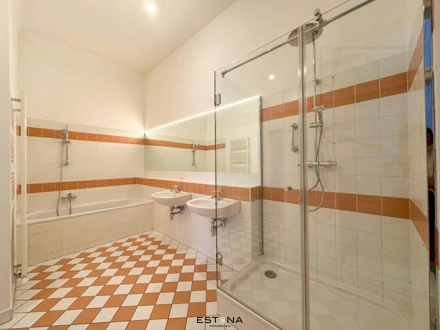 Geräumiges Badezimmer mit Dusche, Badewanne, Doppelwaschbecken und auffälligen orange-weißen Fliesen.