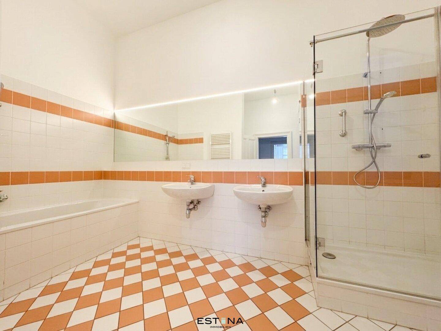 Geräumiges Badezimmer mit Dusche, Badewanne, Doppelwaschbecken und auffälligen orange-weißen Fliesen.