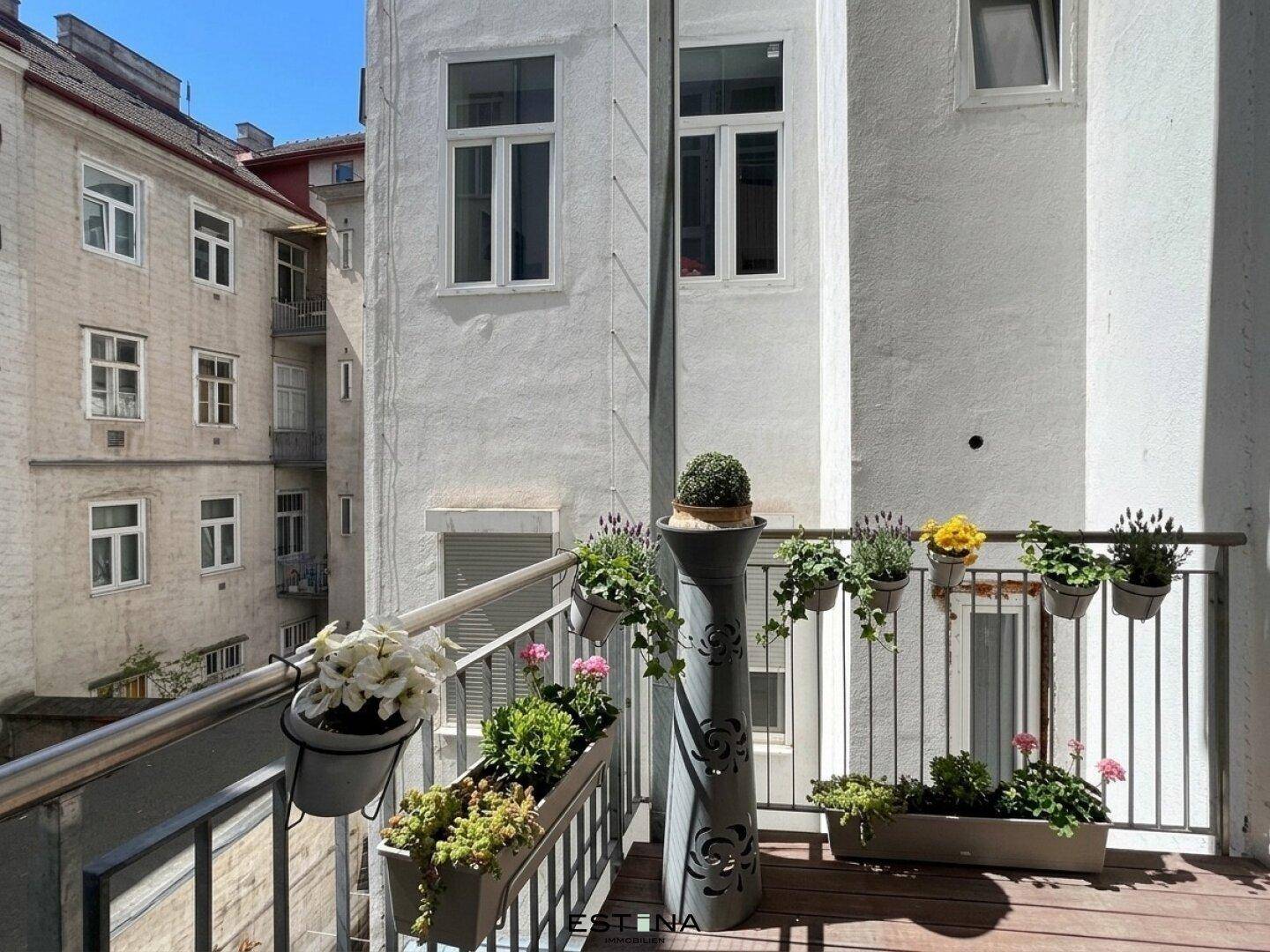 Sonniger Balkon mit Holzboden und vielen Pflanzen, bietet einen Blick auf den Innenhof.