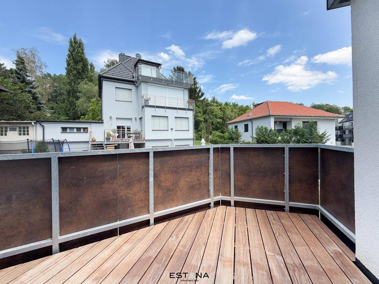 Balkon mit Holzboden und Blick auf die umliegenden Häuser und viel Grün.
