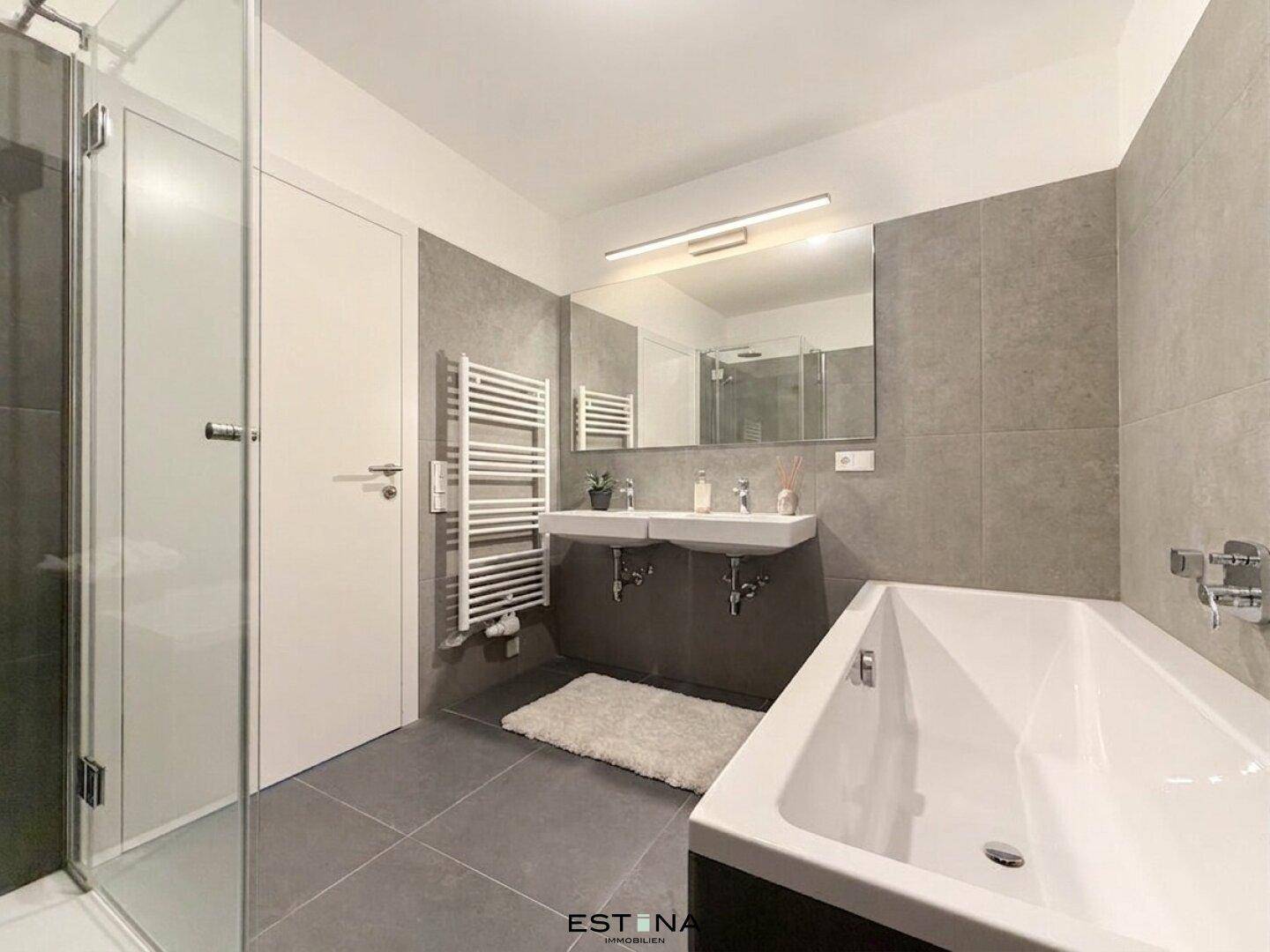 Modernes Badezimmer mit Doppelwaschbecken, Badewanne und separater Dusche, in Grautönen gehalten.