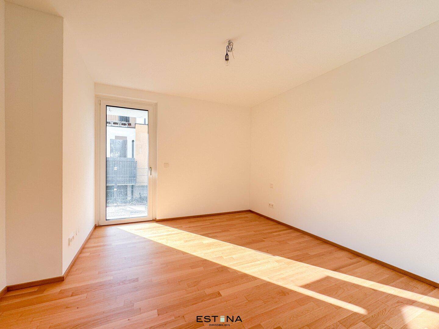Geräumiges Schlafzimmer mit Holzboden und viel Tageslicht durch die Balkontür.